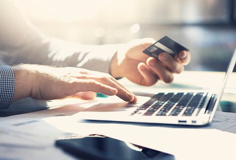 Hands at a laptop, one of them holding a credit card.