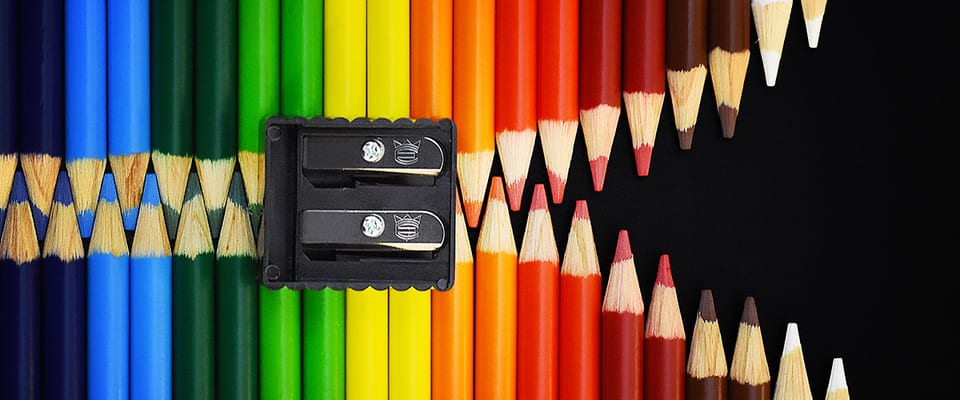 Coloured pencils fanned across a black surface beside a sharpener.